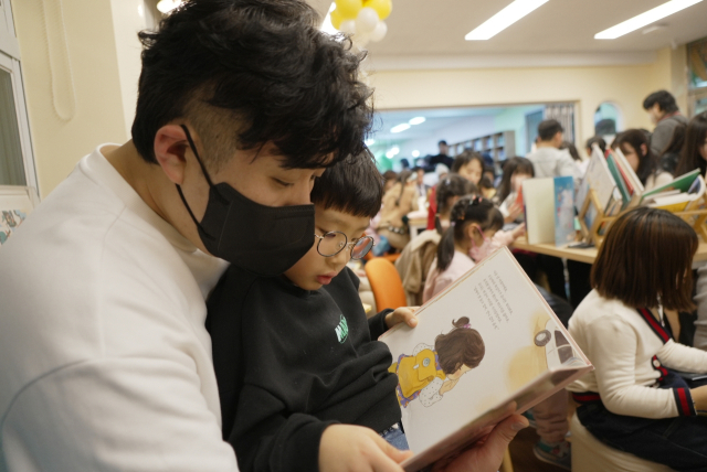 지난 9일 오후 부산 중구 보수초등학교 별빛도서관에서 한 초등학생이 아빠 품에 안겨 동화책을 읽고 있다. 부산시교육청 제공