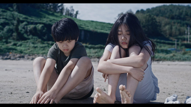 영화 ‘보이 인 더 풀’에서 우주(왼쪽·양희원)가 석영(이예원)에게 물갈퀴를 들키지 않기 위해 발을 모래로 덮고 있는 모습. (주)트리플픽쳐스 제공