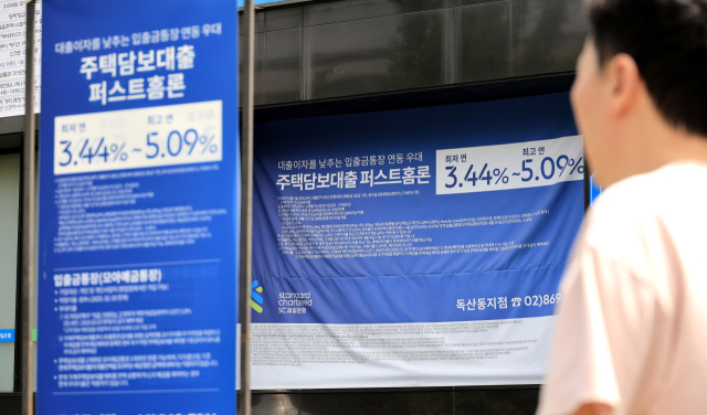 정부는 27일 ‘긴급 가계부채 점검회의’를 개최하고 강도 높은 가계부채 관리방안을 발표했다. 시내 은행 앞 대출 홍보물을 지나는 시민. 연합뉴스