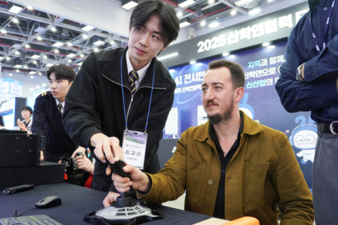 산학연협력 EXPO에서 신라대 학생이 외국인 참여자에게 시뮬레이터 체험을 알려주고 있다.