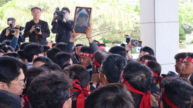 지난 21일 오전 경남 창원시 의창구 경남경찰청 청사 앞에서 화물연대 조합원들과 경찰이 대치했다. 한 화물연대 조합원이 지난 20일 집회 중 사고로 목숨을 잃은 조합원 사진을 들고 있다. 최환석 기자