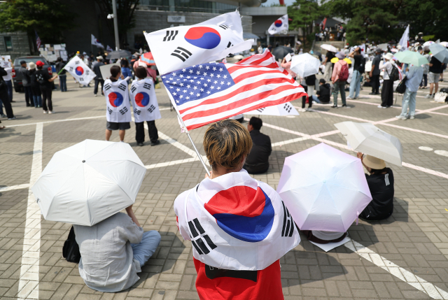 6·3 지방선거 투표용지 부족 사태를 규탄하며 재선거를 요구하는 '잠실 개표소 봉쇄 시위'가 계속되고 있는 9일 서울 송파구 올림픽공원 핸드볼경기장에서 한 참가자가 태극기와 성조기를 흔들고 있다. 연합뉴스